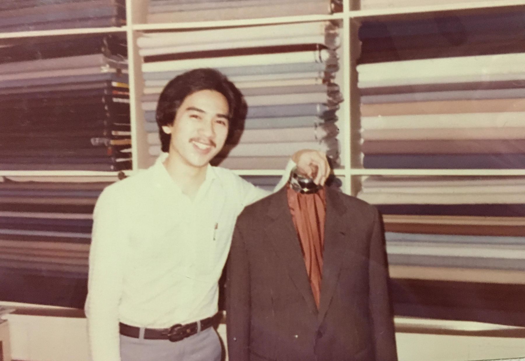 Richard Fan holding a finished bespoke jacket in front of the cloth wall